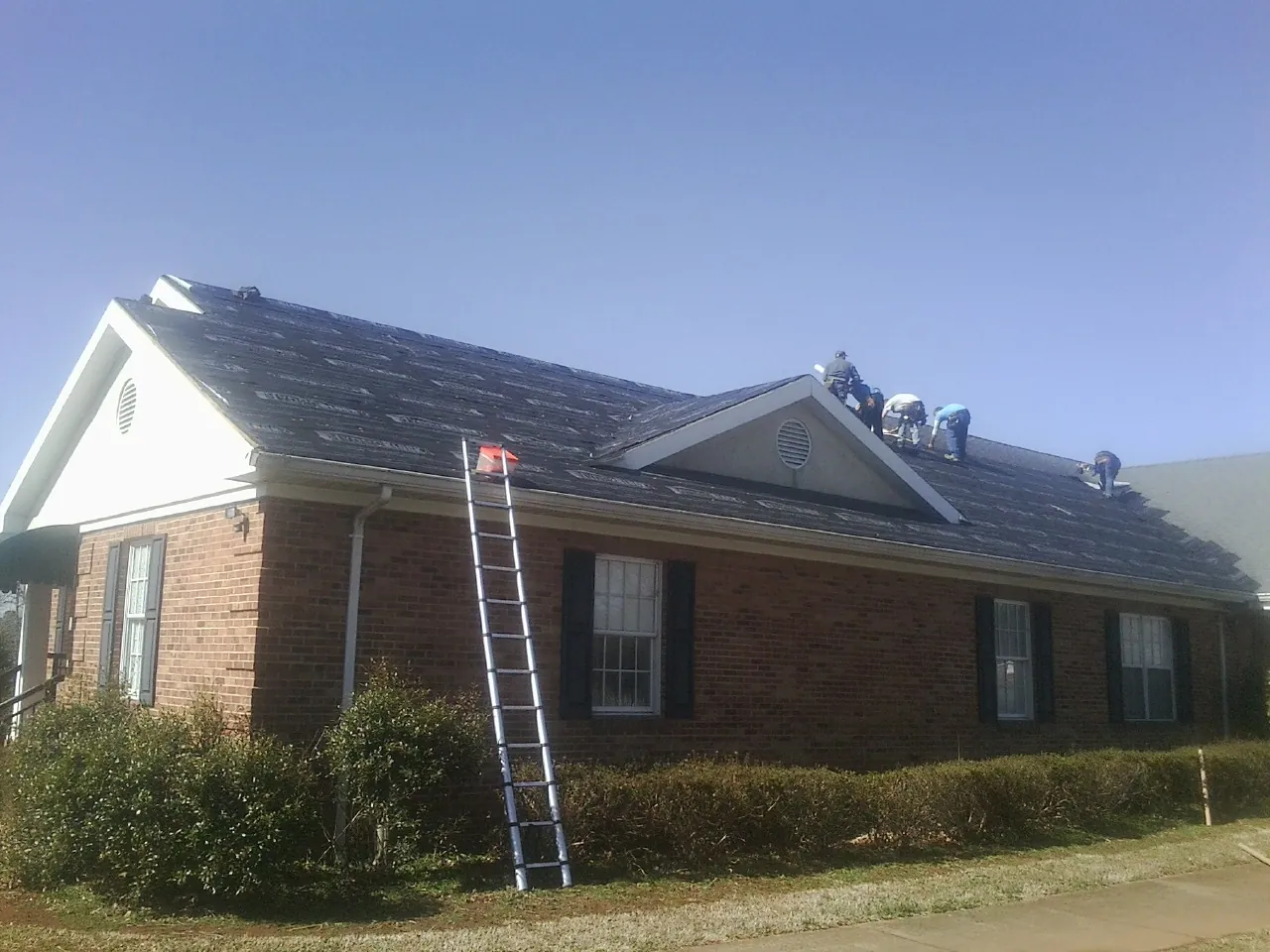 Crew tearing shingles off a brick ranch roof with a ladder set — Emergency Roof Repair work by our crew in Perryopolis