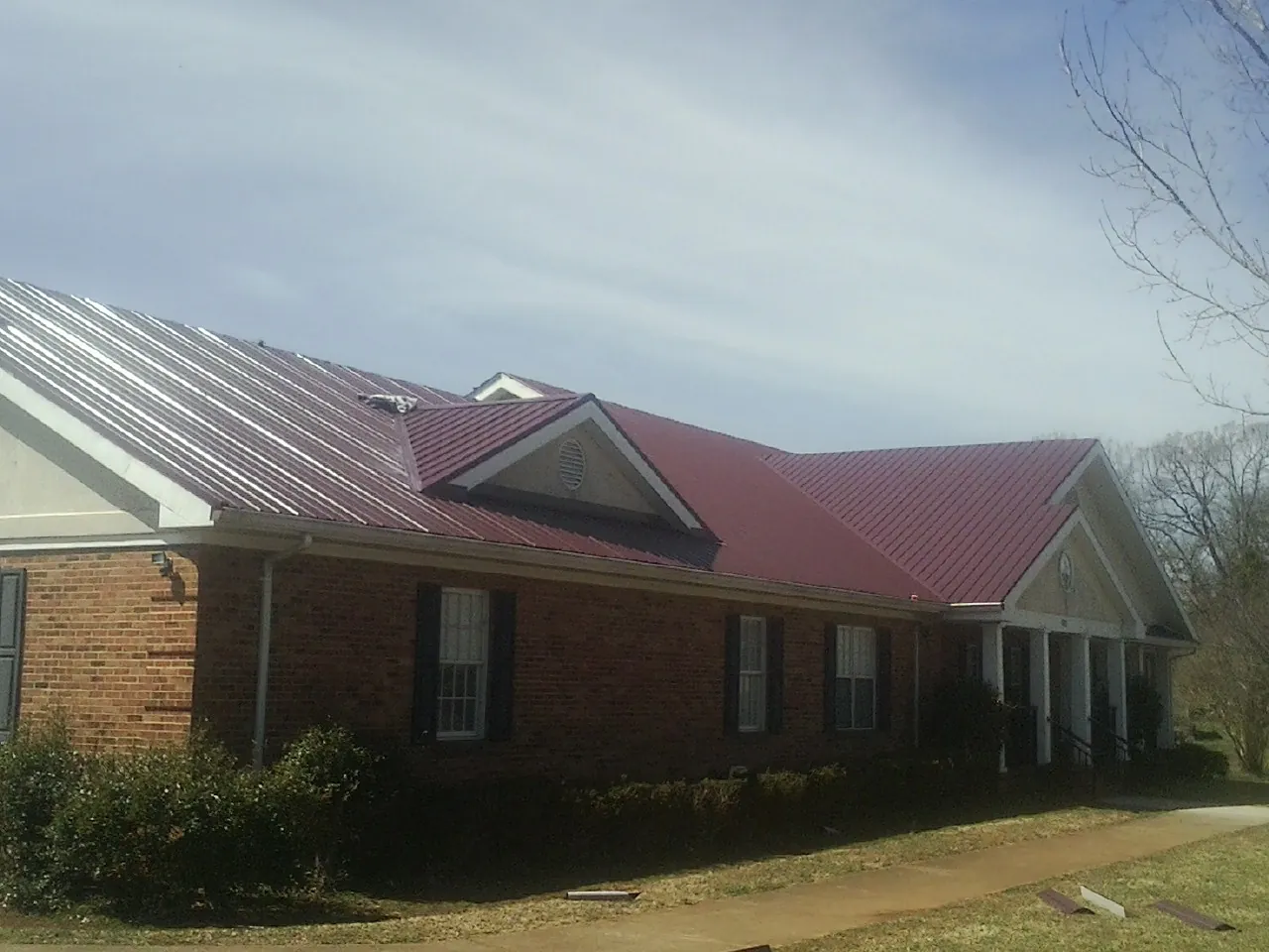 Red metal roof with gabled entries on a long brick building, from a Hail Damage Roof Repair job in Perryopolis