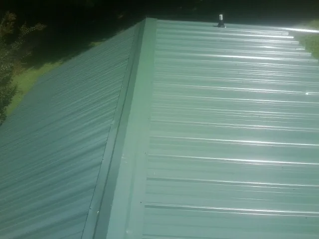 New green metal panels meeting at the ridge of a roof — Flat Roof Repair work by our crew in Perryopolis