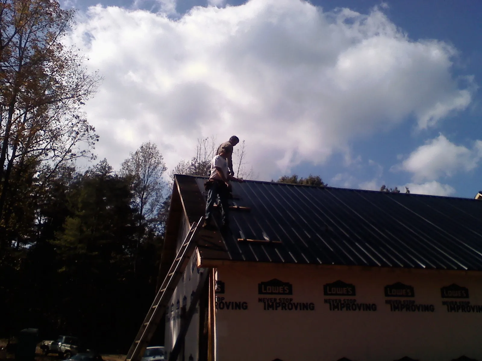 Roofer fastening dark metal panels high against a cloudy sky, from a Roof Inspection job in Perryopolis