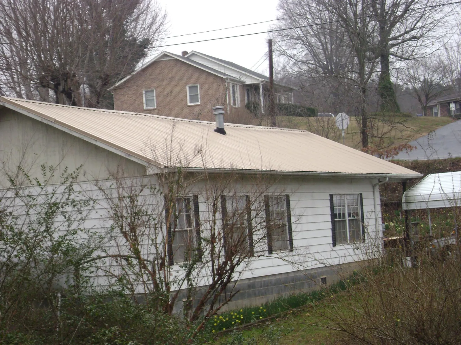 Tan metal roof on a white sided house set into a hillside — Commercial Roofing by Roofing Brothers in Perryopolis